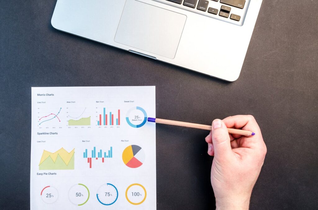 Hand holding pencil reviewing colorful data charts on desk with laptop.